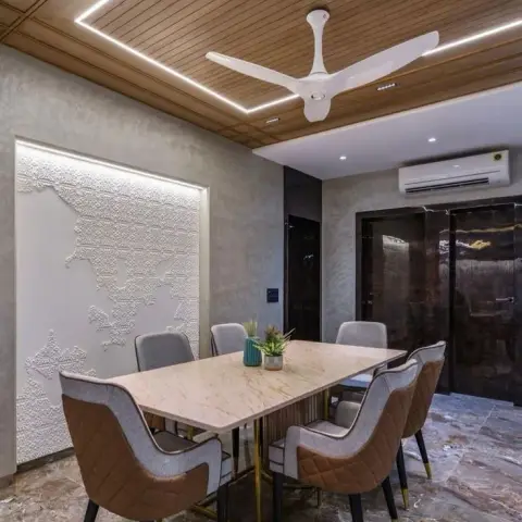 Dining room with a wood-slat cove-lit ceiling, a 3D textured decorative wall panel, and a marble-top table with quilted brown-and-grey chairs.