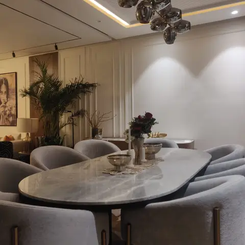Dining room with an oval grey marble table, boucle chairs on brass legs and a sculptural chrome bubble chandelier against panelled walls