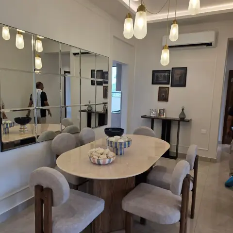 Dining room with an oval stone-top table and sculptural upholstered chairs beneath a cluster of brass-capped glass pendant lights