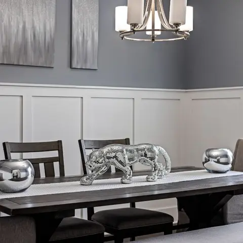 Dining room with grey wainscot wall panelling, a five-arm chandelier and a dark wood table styled with mirrored decor sculptures.
