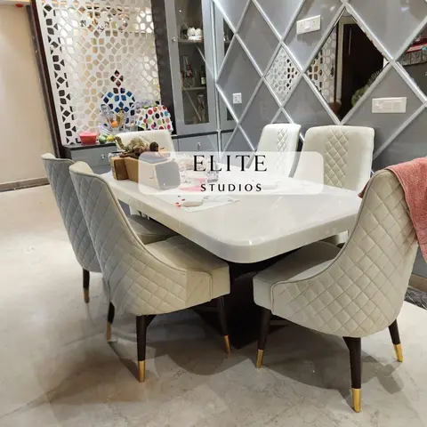 Dining room with quilted cream upholstered chairs on brass-tipped legs, a white marble-top table