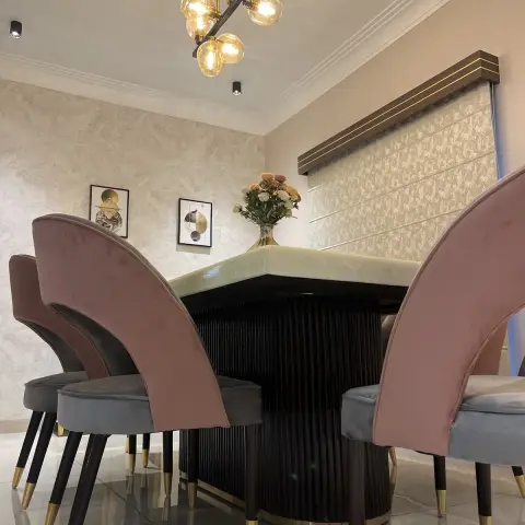 Dining set shot low past dusty-pink and grey velvet chairs to a pale onyx-top table on a fluted black drum pedestal with a brass base band