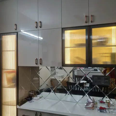 Dining-side crockery unit in greige gloss with rose-gold handles, its centre bay glowing behind bronze reeded glass