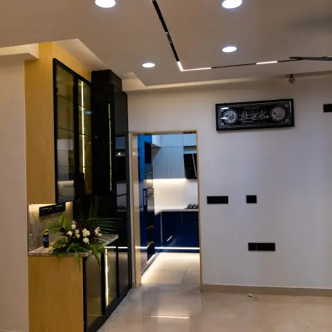 Dining side of a newly finished flat at night — a black steel-framed glass crockery unit with vertical LED strips and an oak-veneer return over a stone-topped