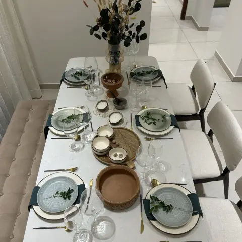 Dining table elaborately laid for a dinner party with sage-green stoneware plates, gold cutlery, terracotta bowls, and a dried-eucalyptus centerpiece