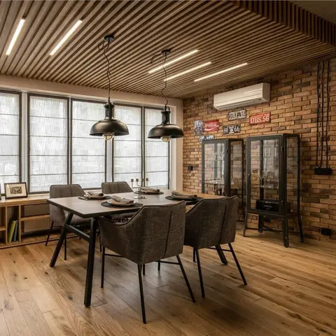 Dining table under twin black dome pendants, set against an exposed brick wall lined with glass display cabinets and a slatted wood ceiling.