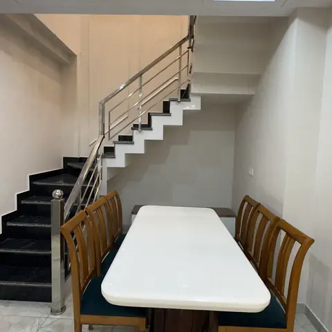 Dining table with a white stone top and turned pedestal base, flanked by wood chairs with teal velvet seats, set beneath an open staircase.