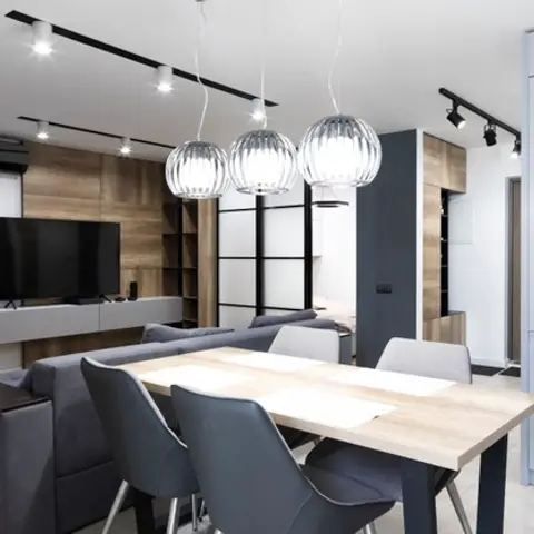 Dining table with grey chairs beneath three glass globe pendants, opening to a sofa and wood-panelled TV wall beyond.
