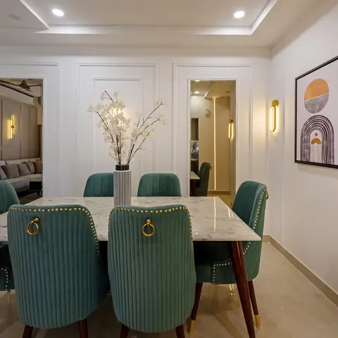 Dining table with marble top and teal ribbed velvet chairs with brass stud trim, set against white wall panelling and a graphic sunrise print