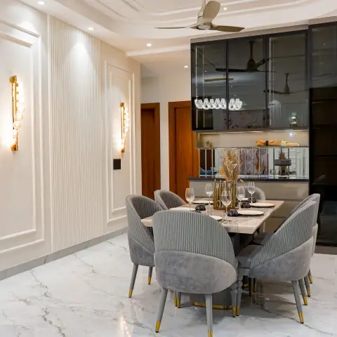 Dining table with six pleated grey velvet chairs under a fluted panel wall, flanked by vertical gold bubble wall sconces and a black-mirrored crockery unit