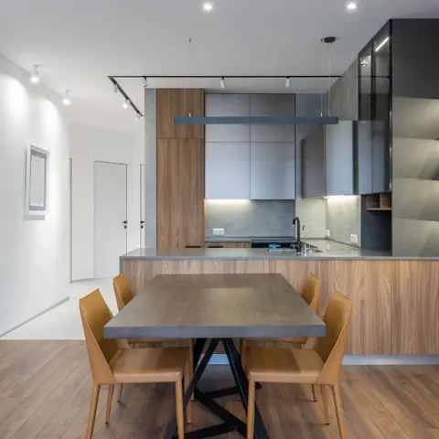 Dining table with tan leather chairs set in front of an open kitchen with walnut and matte-grey cabinetry, a concrete-look backsplash