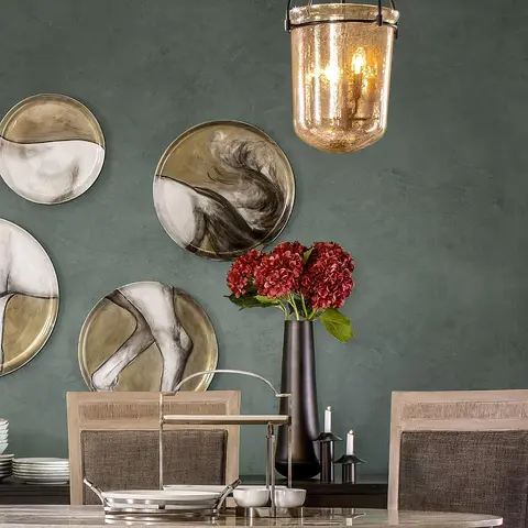 Dining vignette with abstract brush-painted decorative plates on a deep green textured wall, a hammered-glass lantern pendant light
