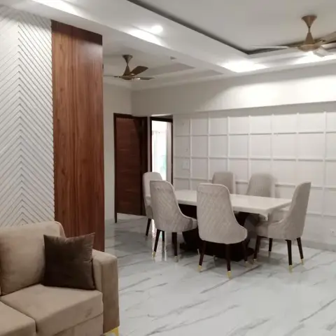 Dining zone on white marble-look flooring with six quilted beige chairs in front of a white square-grid moulding wall