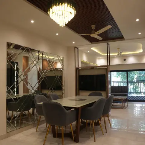 Dining zone under a walnut-slat ceiling raft with a tiered crystal chandelier, six grey brass-legged chairs around a marble-top table