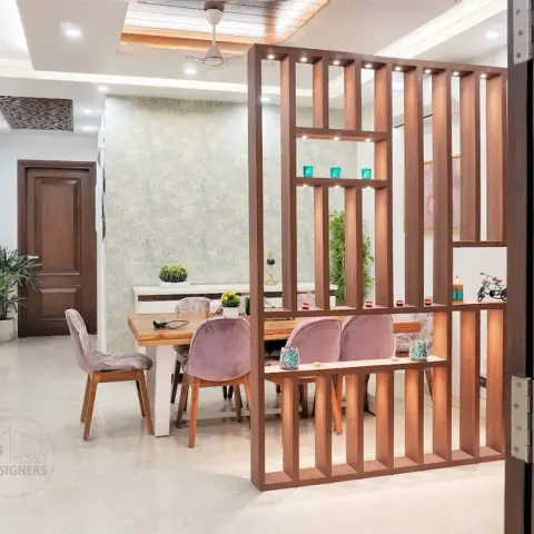 Dining zone viewed through a teak grid partition with lit display shelves, its mauve velvet chairs pulled up to a wood-and-white table against mottled sage