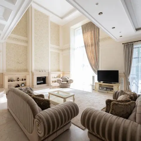 Double-height classic living room with a damask-wallpapered feature wall inside ornate moulded panelling, a fireplace mantel with display shelving