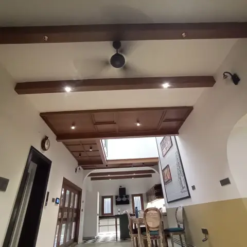 Double-height cream hall under dark-teak beams and a coffered wood ceiling panel, looking past an arch to a checkerboard-floored kitchen