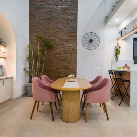 Double-height dining nook with an oval fluted-pedestal table and four dusty-pink velvet chairs set against a split-face stone column