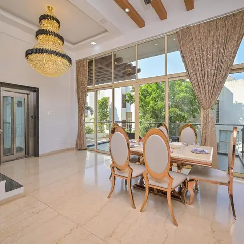 Double-height dining room with a tiered gold-and-black crystal chandelier, oval-back gilt dining chairs around a marble table
