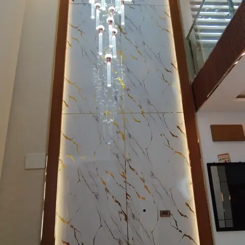 Double-height entrance foyer with a backlit gold-veined marble feature wall, a long cascading crystal chandelier, and a white console below