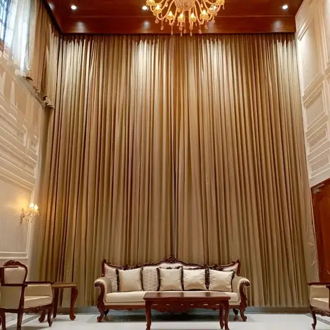 Double-height formal living room with floor-to-ceiling gold silk curtains, a crystal chandelier, a carved wood sofa set, and raised-panel wall moulding.