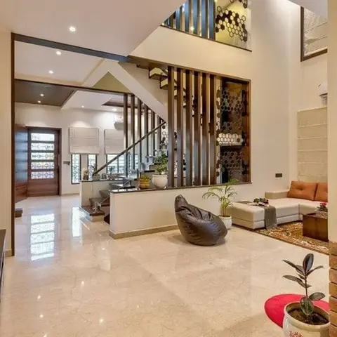 Double-height foyer-living space with a hexagonal metal-and-mirror jaali screen beside the staircase