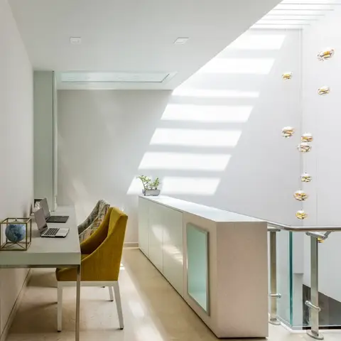 Double-height landing nook with a built-in desk, mustard-yellow chair, and a long strand of hanging glass-orb pendant lights over a glass-railed stairwell.