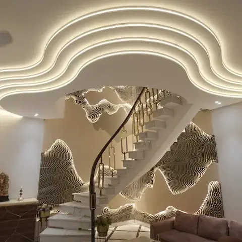 Double-height living area where a backlit CNC contour wall climbs alongside the staircase, under a nested wavy POP ceiling with an LED strip in every reveal.
