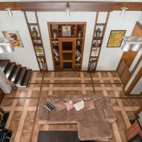 Double-height living room seen from above, with a checkerboard terracotta-and-brown tile floor, exposed wood ceiling beams