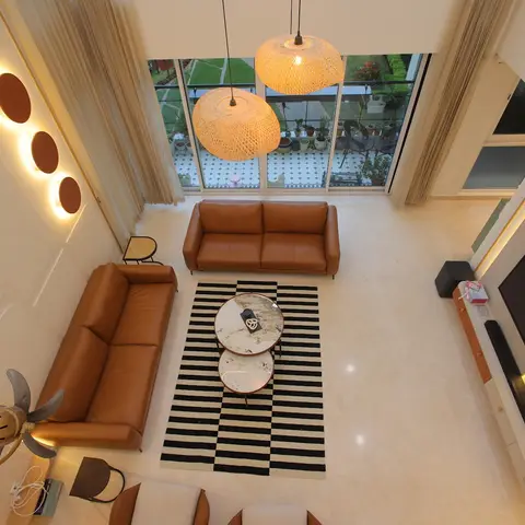 Double-height living room viewed from above, with tan leather sofas around a black-and-white striped rug, two rattan pendant lamps
