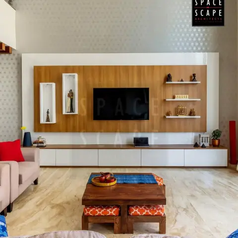 Double-height living room where a teak-veneer TV panel with two white display niches and three floating shelves sits over a wall-hung white console