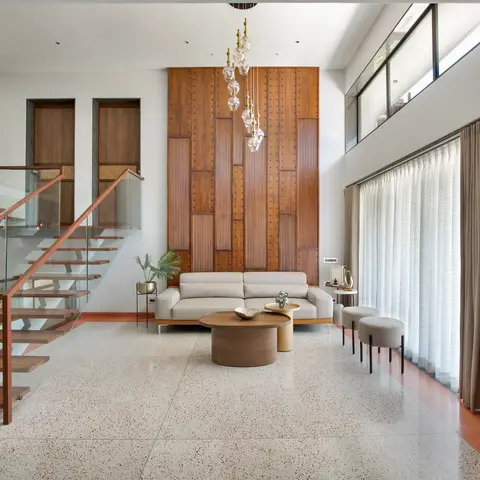 Double-height living room with a floor-to-ceiling fluted teak feature wall, terrazzo flooring and an open wood-and-glass staircase.