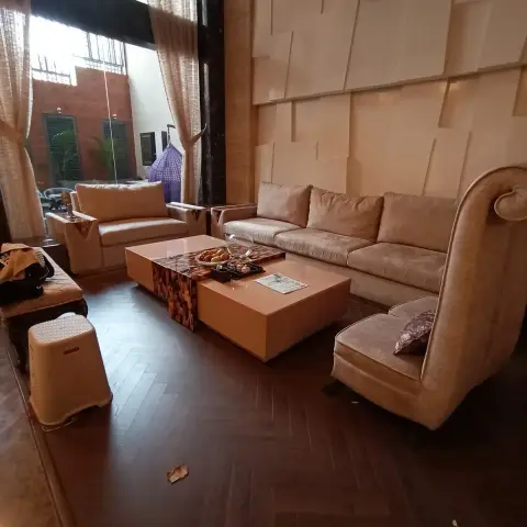 Double-height living room with a 3D textured feature wall, herringbone dark wood flooring, a beige sectional sofa, and a scroll-arm wingback chair.
