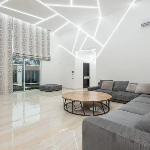 Double-height living room with a geometric LED light-strip ceiling design, a swirl-patterned wallpaper accent wall, a grey L-shaped sectional sofa