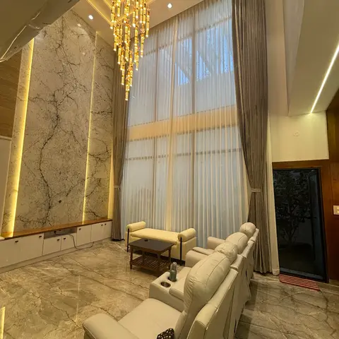 Double-height living room with a book-matched marble feature wall, a spiral crystal-drop chandelier, floor-to-ceiling sheer and blackout curtains
