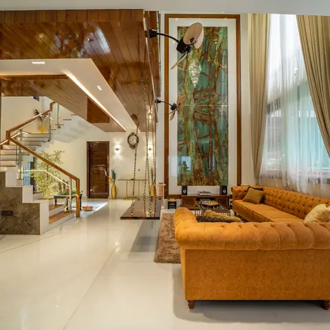 Double-height living room with a backlit green onyx wall panel, a mustard leather chesterfield sofa, and a wood-clad staircase beside a private elevator.