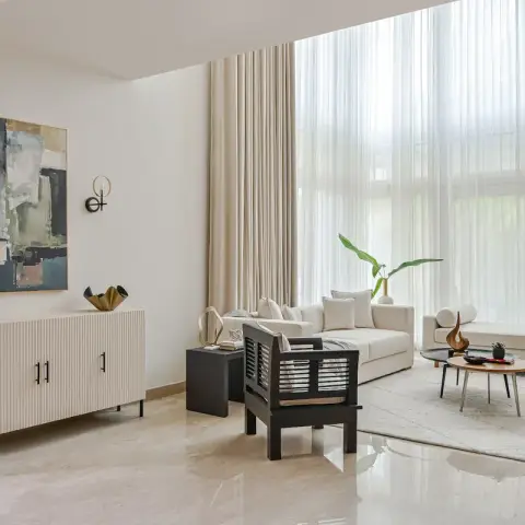 Double-height living room with a fluted white console under an abstract painting, a black wood armchair, cream sofa