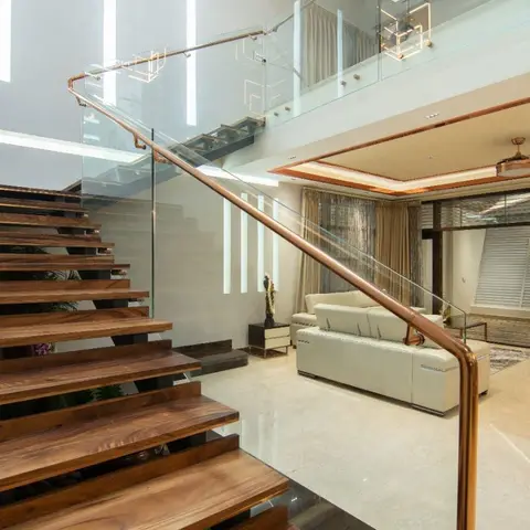 Double-height living room with a floating wood staircase behind a glass-and-copper railing, geometric copper cube pendant lights, a cream leather sofa