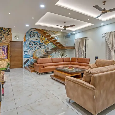 Double-height living room with a hand-painted blue peacock mural along the staircase wall, tan and brown leather sofas, a glass-top coffee table