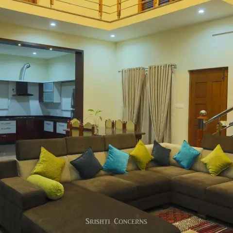 Double-height living room with an L-shaped brown sectional sofa styled with teal, olive and grey cushions, a glass water-feature column divider