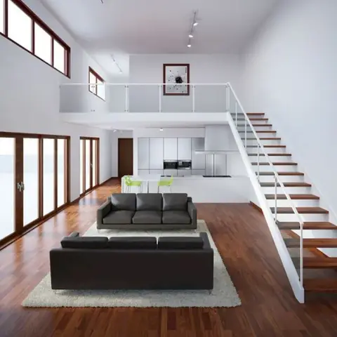 Double-height living room with dark leather sofas facing a floating staircase and open mezzanine landing