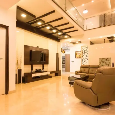 Double-height living room with staggered dark-wood ceiling battens carrying spotlights, a TV on a dark veneer panel