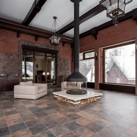 Double-height living space with exposed brick walls, dark timber beams, a central suspended fireplace on a stone hearth