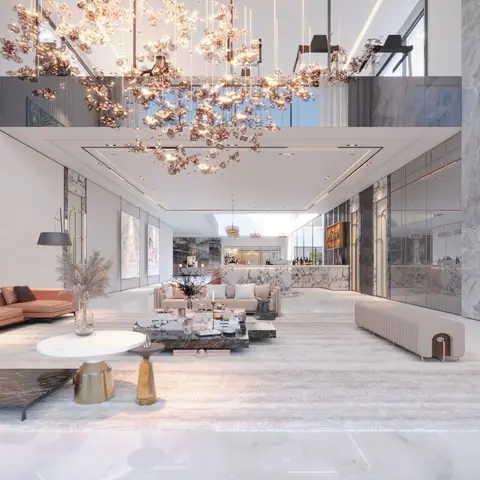 Double-height luxury lounge with a large floral crystal chandelier, marble flooring and cladding, and blush leather sofas around dark marble coffee tables.