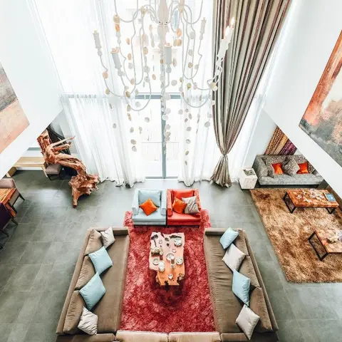 Double-height open-plan space viewed from a mezzanine, showing a dining table, two separate lounge seating groups on layered rugs