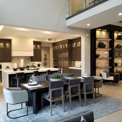 Double-height open-plan space with a dark wood kitchen and waterfall-edge island on one side, a dining table with upholstered chairs in the centre