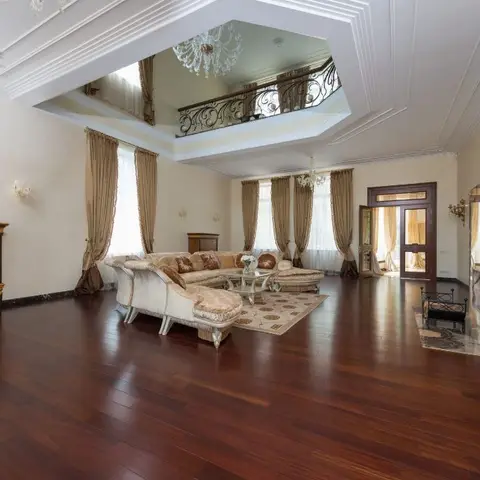 Double-height opulent living room with dark hardwood flooring, an ornate gilded ceiling opening to a wrought-iron mezzanine railing