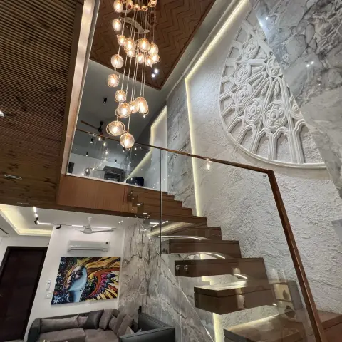 Double-height stairwell with a cascading cluster-glass pendant chandelier under a chevron wood ceiling, a carved marble jaali medallion wall