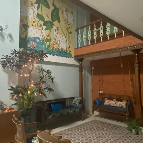 Double-height traditional sitting area with a hand-painted mural of cows and lotus flowers, a carved wooden hanging swing with blue and floral cushions
