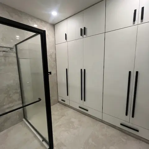 Dressing area with a full-height white wardrobe wall in black bar handles opening directly onto a black-framed glass walk-in shower enclosure